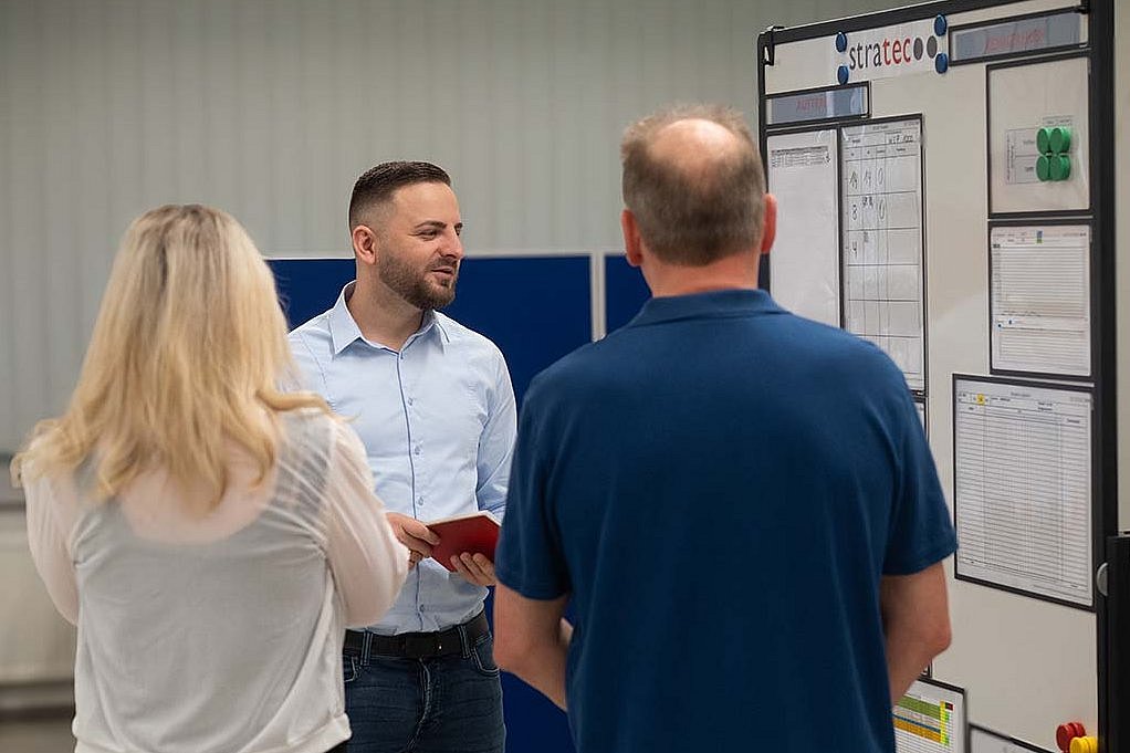 Two colleagues from STRATEC standing in front of Ali while he is showing something on the flipchart