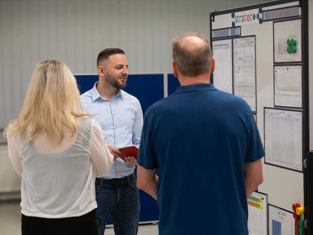 Two colleagues from STRATEC standing in front of Ali while he is showing something on the flipchart