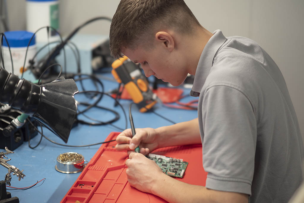 Yoann from STRATEC assemblying a module with workshop equipment on his right side and a lamp shining on the module from the left side 