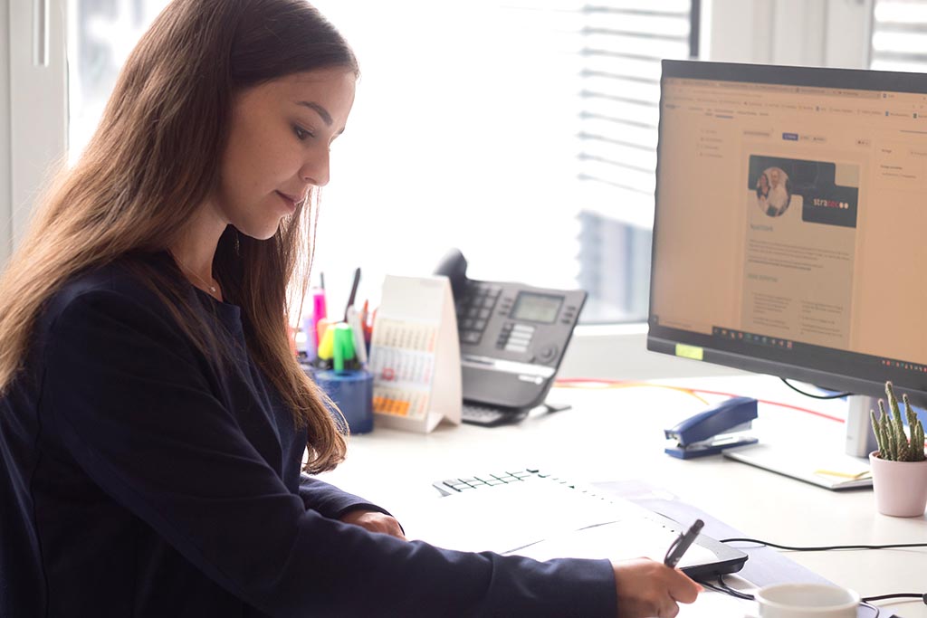 Hanna from STRATEC noting something into her notebook while sitting on her desk with a monitor and desk utensils