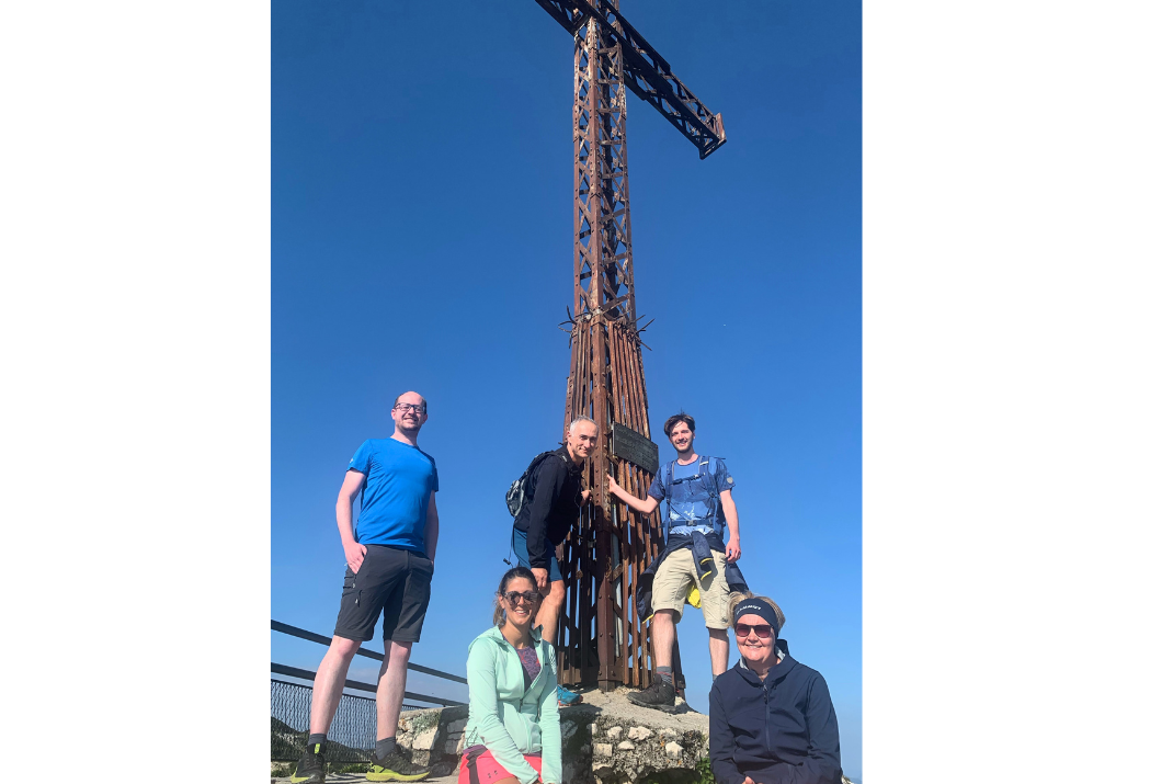 Selfie of our STRATEC employees on a team hike in front of a metal cross in Austria 