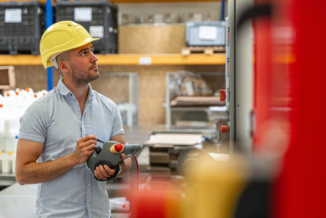 Berti from Diatron in the production hall with a yellow safety helmet operating a machine