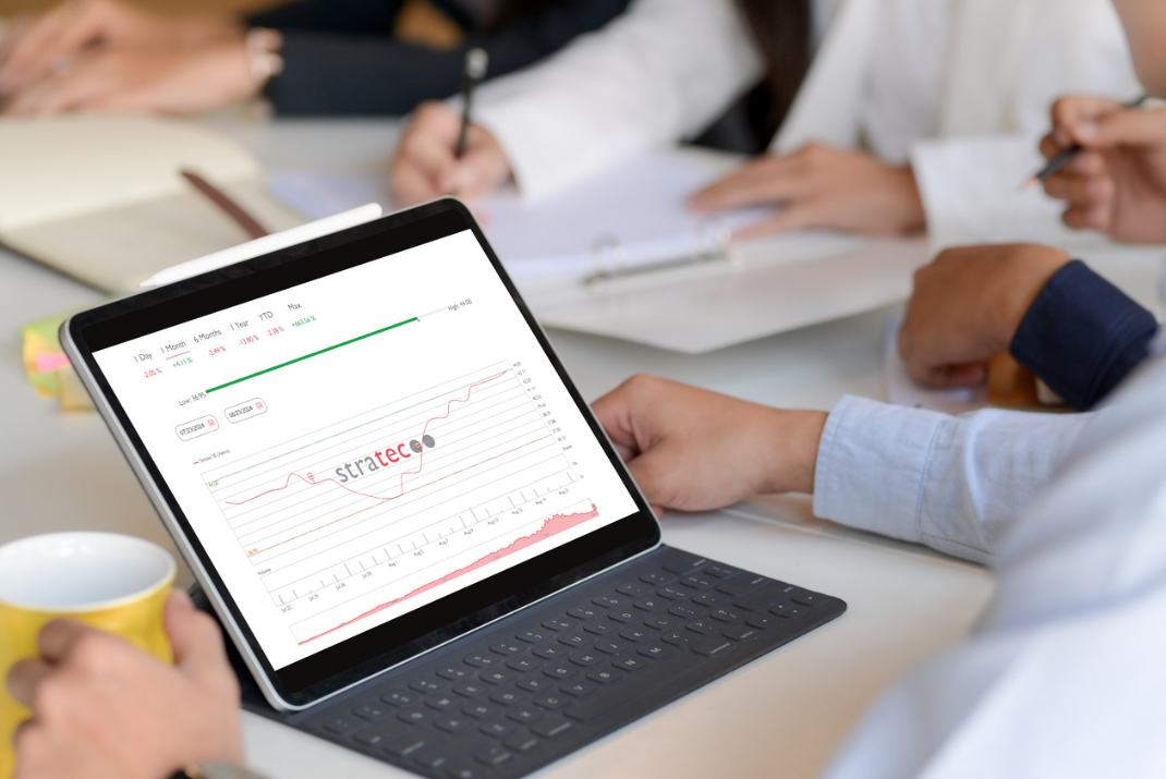 Employees sitting on a desk with a tablet that shows the stock information of STRATEC