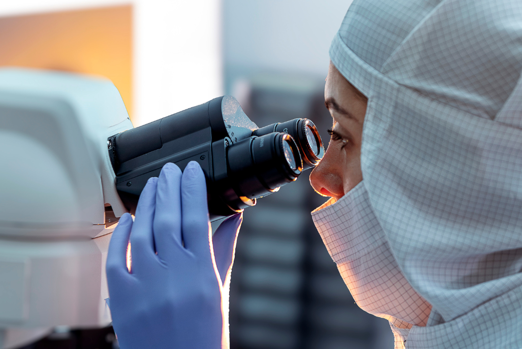 STRATEC employee with safety gloves and head cover looking into a microscope